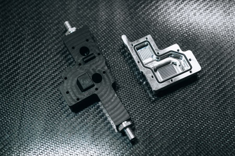 Two machined liquid-cooling blocks for the Revolve NTNU car on a carbon-fibre surface